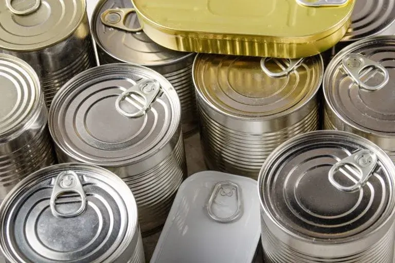 Latas de alimentos en diferentes tamaños y colores, incluyendo latas metálicas y una lata dorada en la parte superior. Ideal para ilustrar la conservación de alimentos y productos enlatados.
