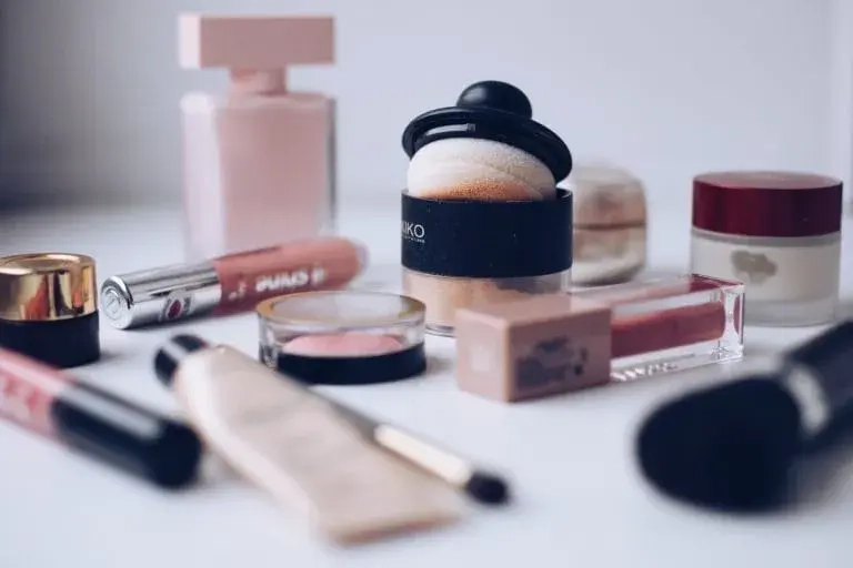 Imagen de productos de maquillaje sobre una superficie clara, incluyendo bases, labiales, sombras de ojos y un perfume. Los envases son de tonos suaves y elegantes, ideales para una rutina de belleza. Perfecto para amantes del maquillaje y tendencias de cosmética.