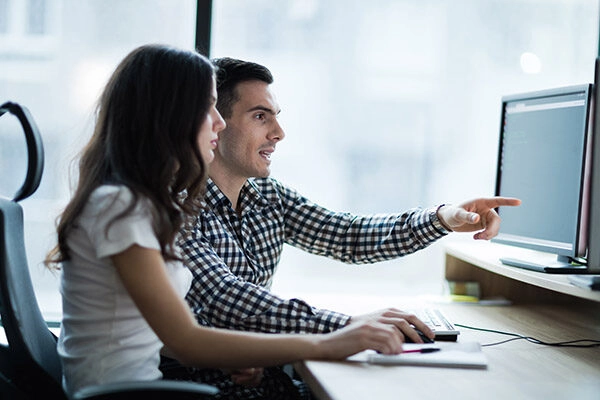Dos profesionales colaborando en un entorno de oficina, uno de ellos señala la pantalla de un ordenador mientras la otra persona observa. La imagen refleja trabajo en equipo y comunicación en un proyecto digital. Ideal para destacar la importancia de la colaboración en el ámbito laboral.